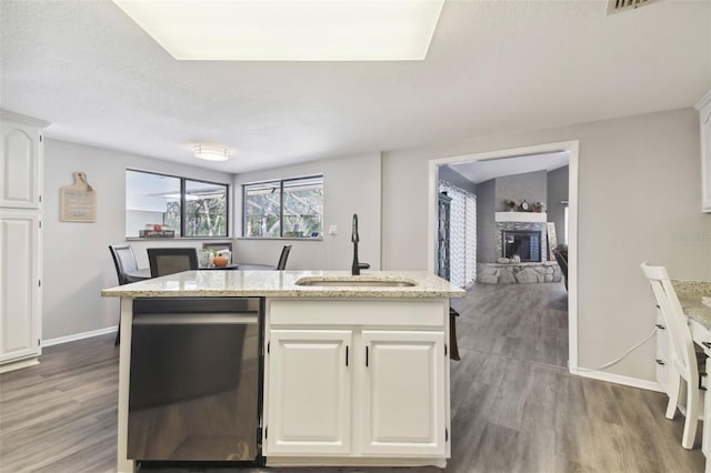 kitchen with a fireplace, hardwood / wood-style floors, an island with sink, and sink