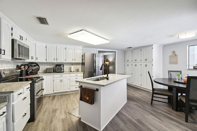 kitchen with sink, light hardwood / wood-style flooring, an island with sink, white cabinets, and appliances with stainless steel finishes