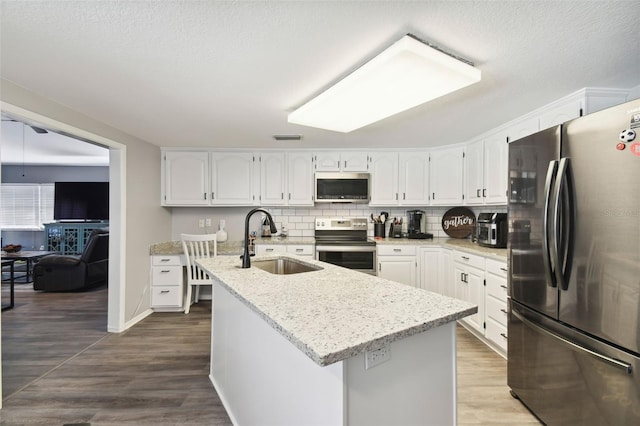 kitchen featuring a kitchen island with sink, white cabinets, sink, hardwood / wood-style flooring, and appliances with stainless steel finishes