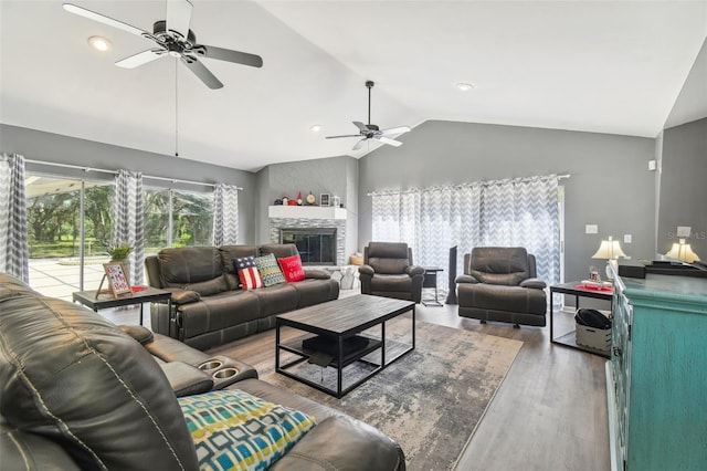 living room featuring ceiling fan, a large fireplace, wood-type flooring, and vaulted ceiling