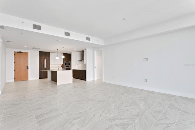 unfurnished living room with baseboards, visible vents, and a sink