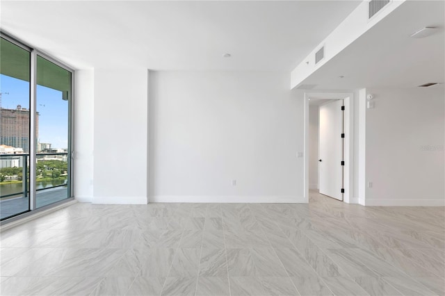 spare room featuring a wall of windows, baseboards, and visible vents