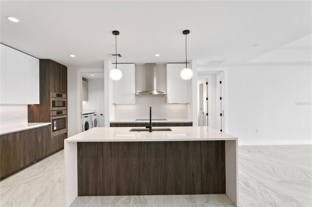 kitchen with hanging light fixtures, wall chimney range hood, dark brown cabinets, white cabinets, and washer and dryer