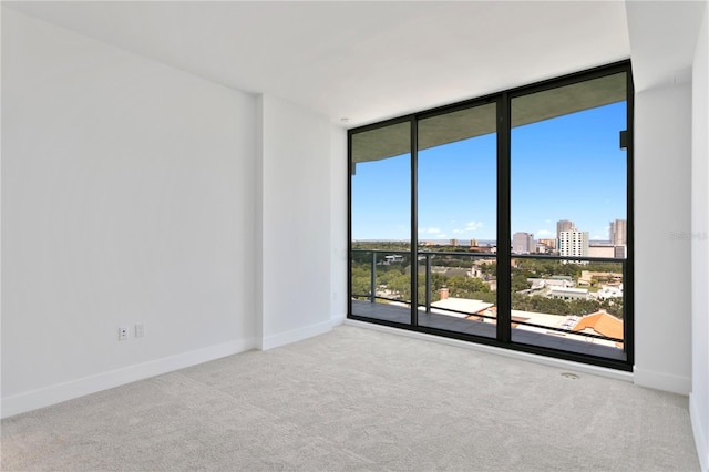 carpeted empty room featuring a view of city, baseboards, and expansive windows