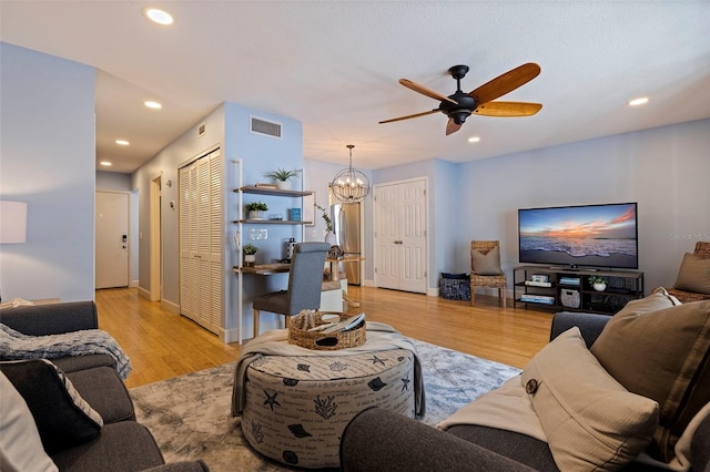 living room with ceiling fan with notable chandelier and light hardwood / wood-style floors