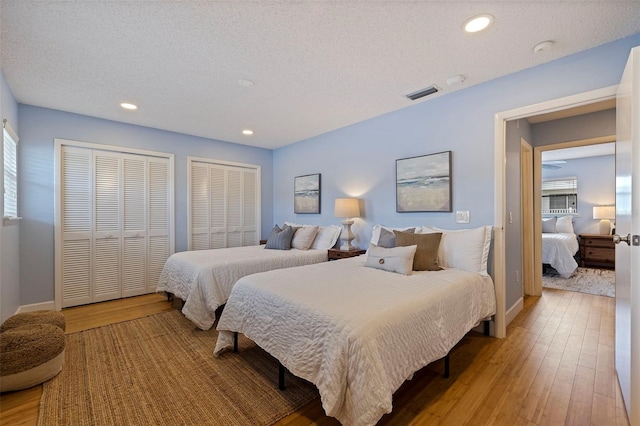 bedroom with multiple closets, a textured ceiling, and light wood-type flooring