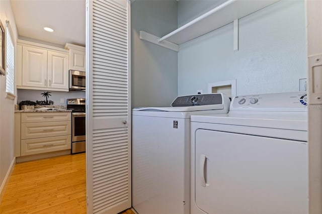 laundry area with washing machine and clothes dryer and light wood-type flooring