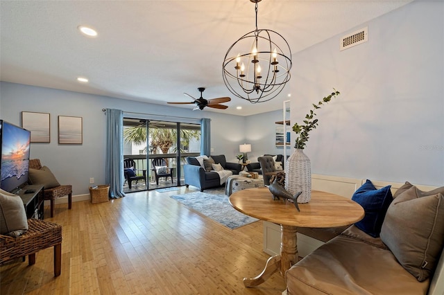 living room featuring ceiling fan with notable chandelier and light hardwood / wood-style flooring