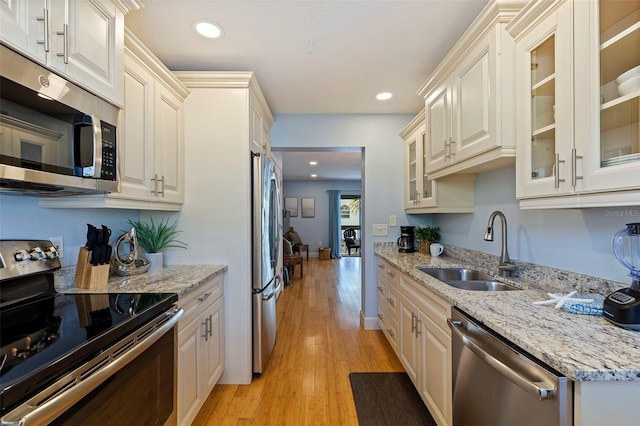 kitchen with light stone counters, sink, stainless steel appliances, and light wood-type flooring