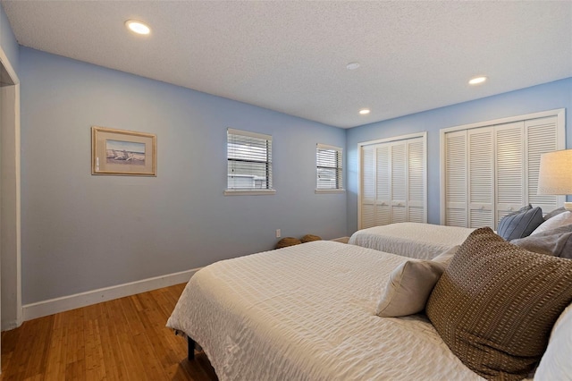 bedroom featuring two closets, light hardwood / wood-style flooring, and a textured ceiling