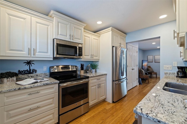 kitchen with light stone countertops, appliances with stainless steel finishes, light wood-type flooring, and sink