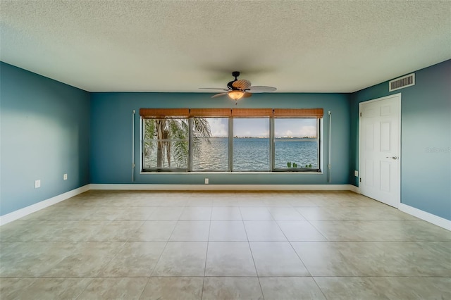 unfurnished room featuring a water view, ceiling fan, a textured ceiling, and light tile patterned floors