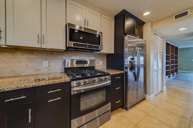 kitchen with appliances with stainless steel finishes, white cabinets, decorative backsplash, light tile patterned floors, and light stone countertops