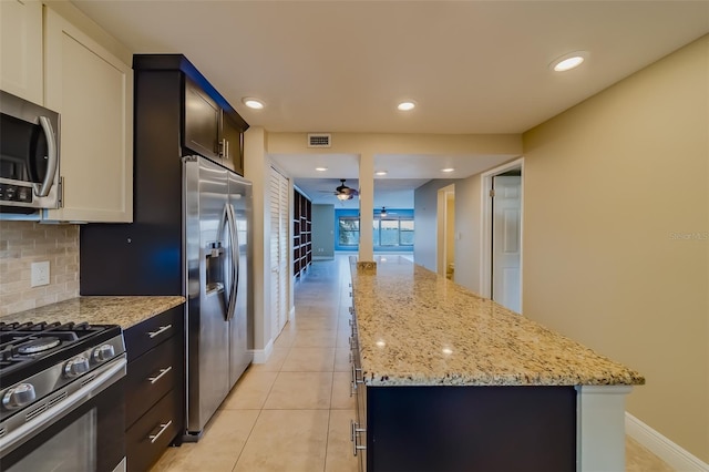 kitchen with a kitchen island, appliances with stainless steel finishes, tasteful backsplash, ceiling fan, and light stone counters