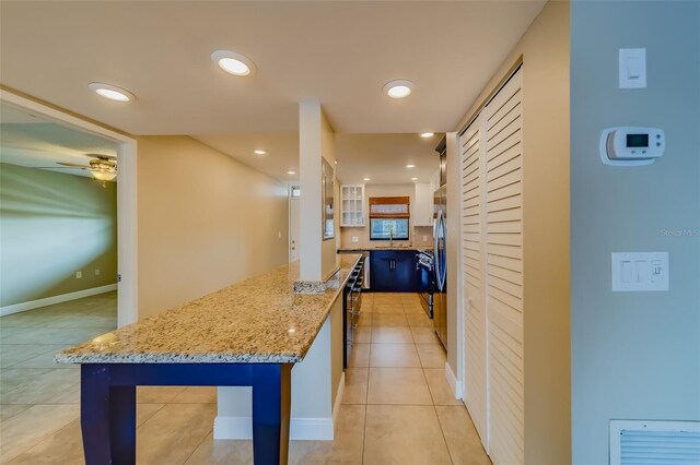 kitchen with ceiling fan, a kitchen breakfast bar, a center island, light stone countertops, and light tile patterned flooring