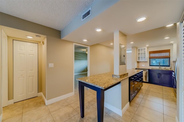 kitchen with light tile patterned flooring, sink, light stone counters, a textured ceiling, and stainless steel dishwasher