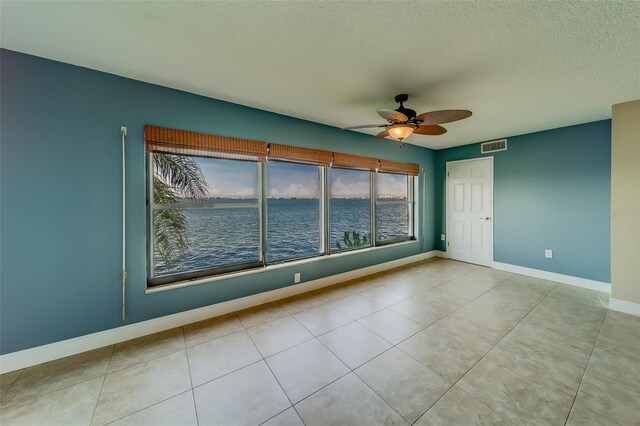 tiled empty room with ceiling fan, a water view, and a textured ceiling