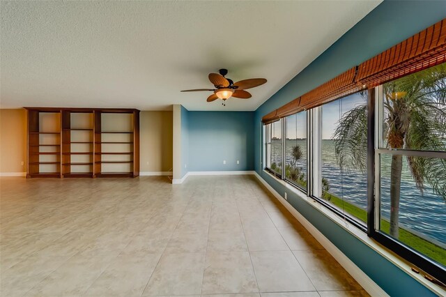 tiled spare room with a textured ceiling, ceiling fan, and a water view