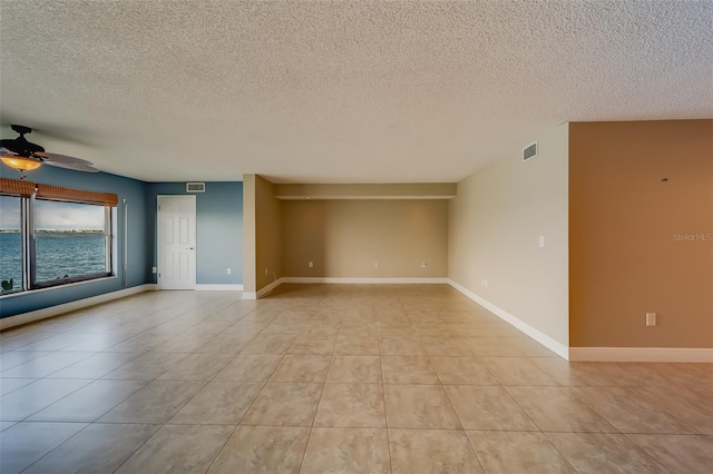 tiled empty room with a water view, ceiling fan, and a textured ceiling