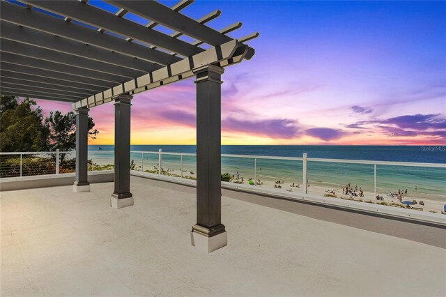 patio terrace at dusk featuring a water view, a beach view, and a pergola