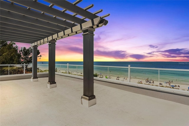 patio terrace at dusk with a view of the beach, a water view, and a pergola