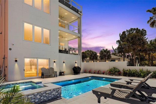 pool at dusk featuring a patio, ceiling fan, and an in ground hot tub