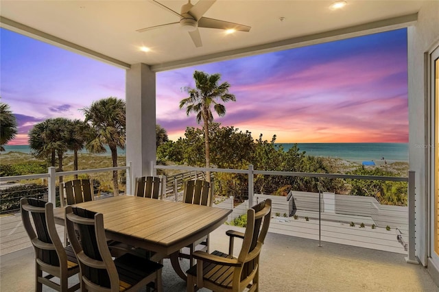 patio terrace at dusk with ceiling fan, a balcony, and a water view