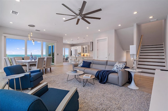 living room featuring ceiling fan, a water view, and light wood-type flooring