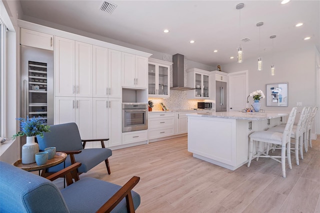 kitchen with white cabinetry, decorative light fixtures, oven, and wall chimney exhaust hood