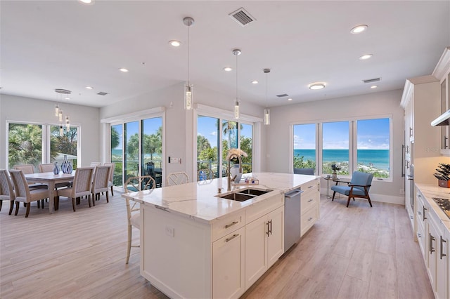 kitchen with appliances with stainless steel finishes, decorative light fixtures, an island with sink, sink, and a water view