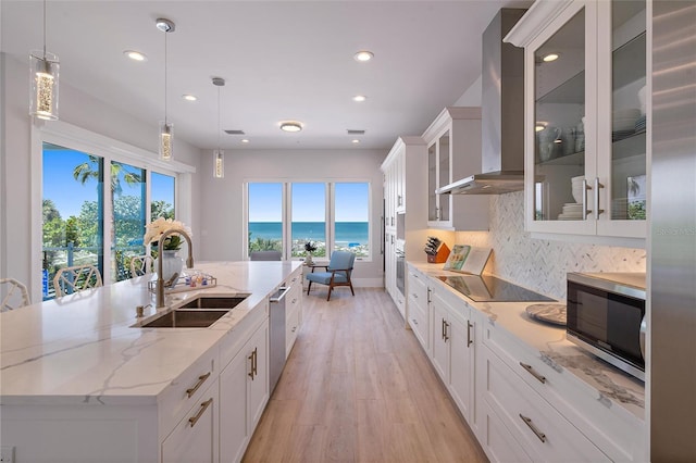 kitchen featuring a spacious island, sink, a water view, stainless steel appliances, and wall chimney range hood