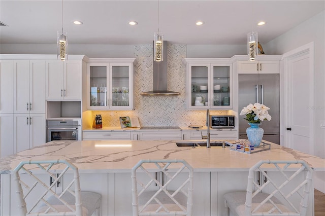 kitchen with wall chimney range hood, decorative light fixtures, a breakfast bar area, and stainless steel appliances