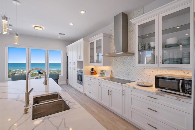 kitchen with pendant lighting, sink, stainless steel appliances, a water view, and wall chimney range hood