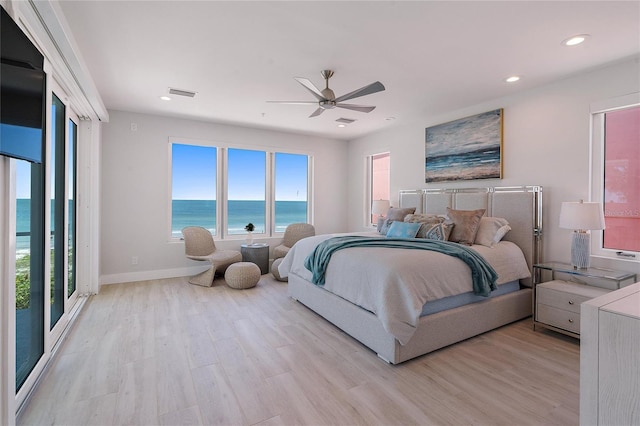 bedroom featuring multiple windows, light hardwood / wood-style flooring, ceiling fan, and a water view