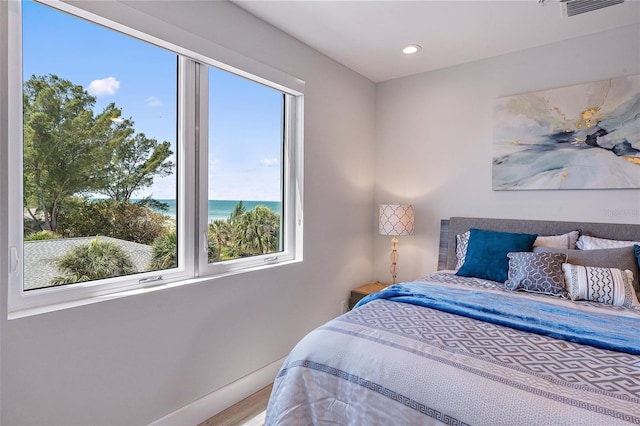 bedroom with multiple windows, hardwood / wood-style floors, and a water view