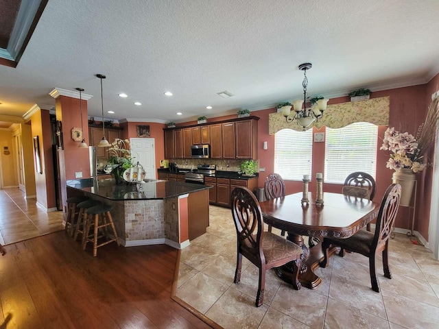 dining area with crown molding, light wood-style floors, visible vents, and an inviting chandelier