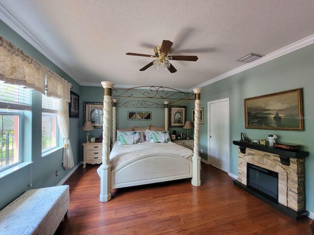 bedroom featuring dark wood-style floors, a stone fireplace, ornamental molding, and visible vents