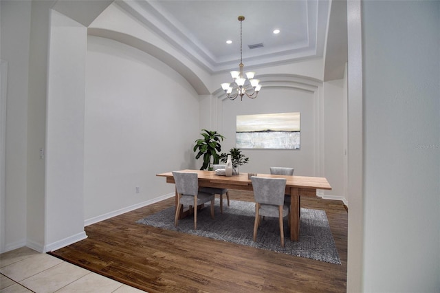 dining space featuring a tray ceiling, a notable chandelier, and light hardwood / wood-style flooring