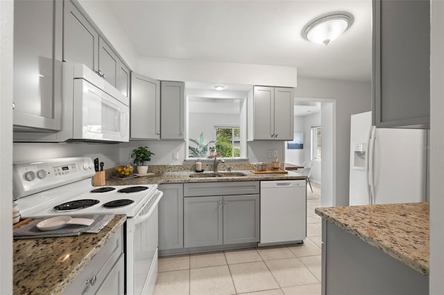 kitchen featuring gray cabinetry, sink, light tile patterned floors, white appliances, and light stone countertops