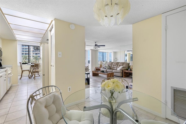 tiled dining room with ceiling fan with notable chandelier and a textured ceiling