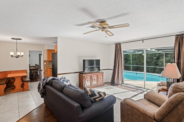 living room featuring a textured ceiling, ceiling fan with notable chandelier, and light tile patterned floors