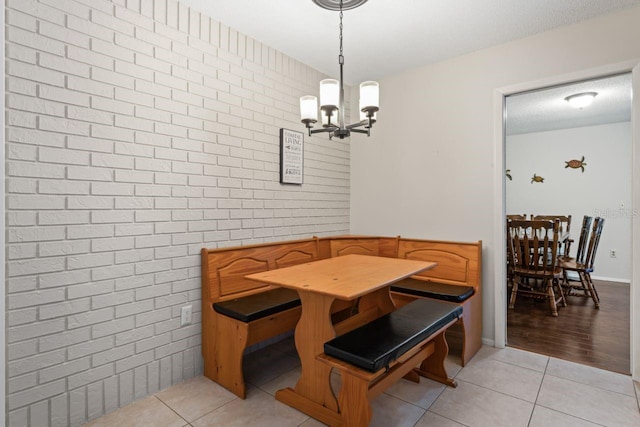 dining area with brick wall, a textured ceiling, light tile patterned floors, and a notable chandelier