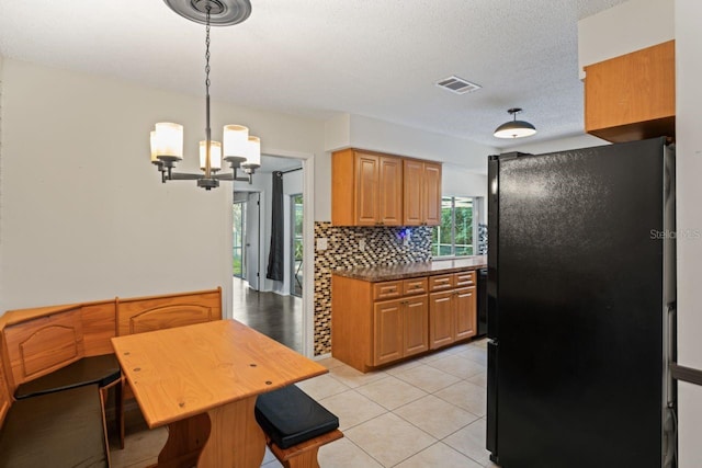 kitchen featuring light tile patterned floors, hanging light fixtures, decorative backsplash, an inviting chandelier, and black refrigerator