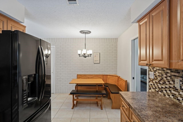 kitchen featuring a textured ceiling, light tile patterned floors, a notable chandelier, black fridge, and brick wall