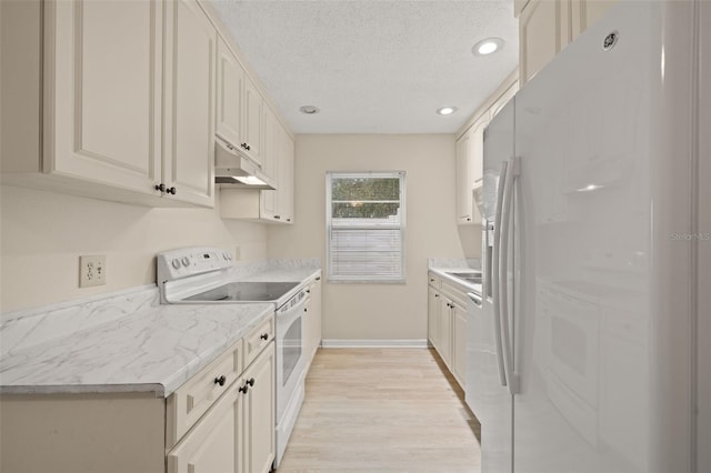 kitchen with light wood-type flooring, white cabinets, white appliances, and a textured ceiling