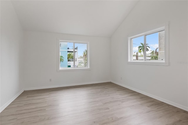 spare room with vaulted ceiling, a healthy amount of sunlight, and light hardwood / wood-style flooring