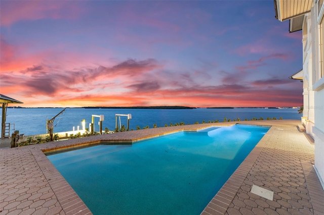 pool at dusk with a patio area and a water view