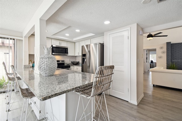 kitchen featuring appliances with stainless steel finishes, a breakfast bar area, tasteful backsplash, white cabinetry, and light hardwood / wood-style flooring