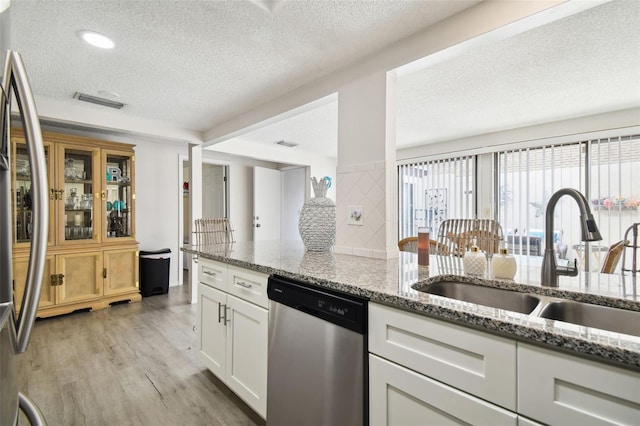 kitchen with white cabinets, stainless steel appliances, light stone counters, and light hardwood / wood-style floors