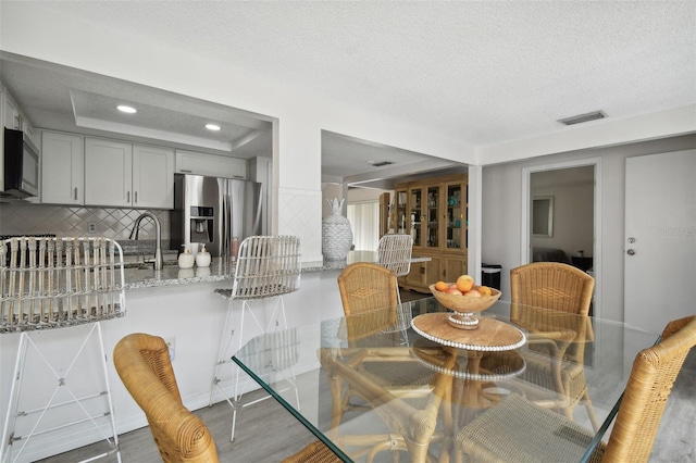 dining space with a textured ceiling, hardwood / wood-style floors, and a tray ceiling